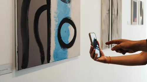 Person photographing abstract painting in art gallery.