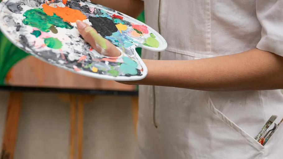 Person holding paint palette, wearing white apron.