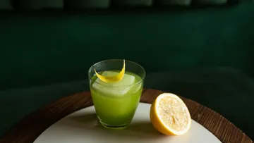 Grüner Cocktail mit Zitronenschale auf Tisch.