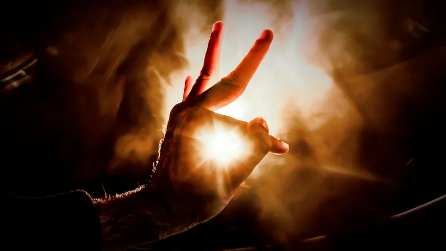 Hand zeigt Peace-Zeichen vor hellem Licht.