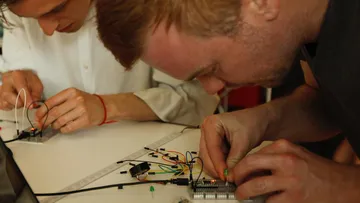 Two people assembling electronics on a table.