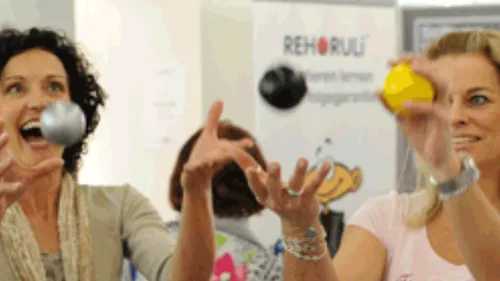 Two women juggling colorful balls indoors.