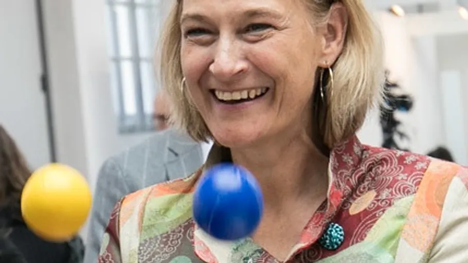 Woman juggling colorful balls indoors, smiling.