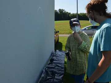 Zwei Personen besprechen das Sprayen an einer Wand.