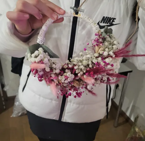 Person holding decorative floral wreath indoors.