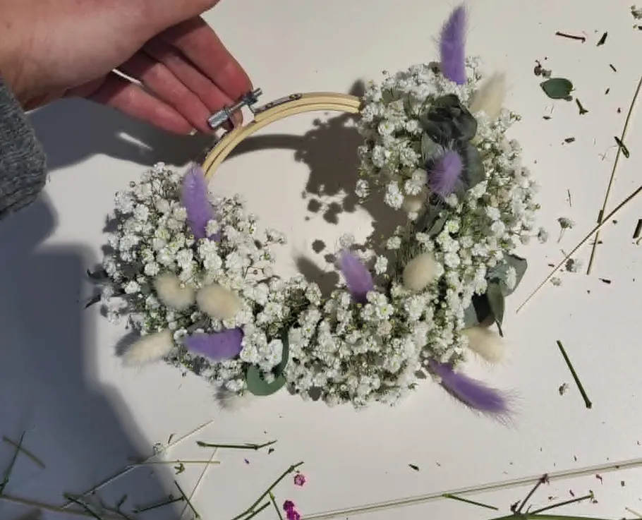 Hand holding flower wreath with white and purple details.