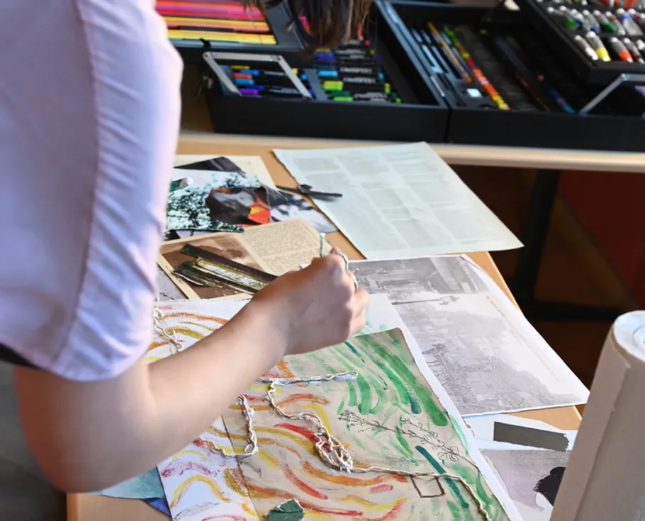 Person crafting collage on a desk with tools.
