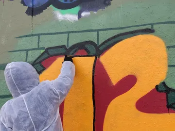 Eine Person sprayt Farbe auf eine Wand.