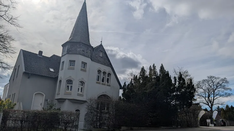 Altes Gebäude mit Spitzdach, bewölkter Himmel.
