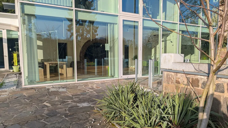Modern glass house with stone patio and plants.