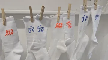 Weiße Socken mit Aufdrucken, hängen an einer Leine.