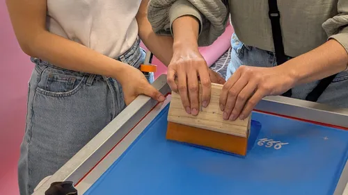 Two people screen printing on blue surface.