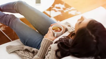 Frau entspannt, hält Zitronentee, auf Sofa.