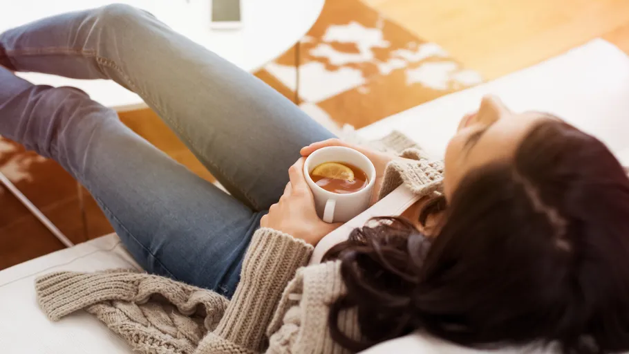 Frau entspannt, hält Zitronentee, auf Sofa.