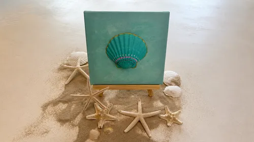 Leinwand mit Muschelgemälde auf Sandoberfläche.
