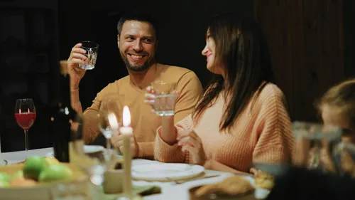 Couple smiling, holding drinks, at dinner table.