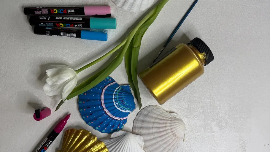 Painted seashells, markers, and a gold bottle on table.