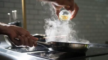 Person pouring liquid into steaming pan on stove.