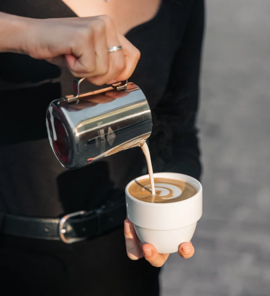 Person gießt Milch in Tasse, Latte Art entsteht.