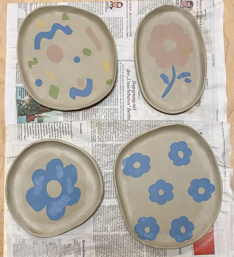Four painted plates with abstract designs on newspaper.