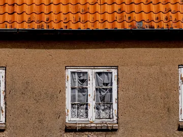 Two windows with curtains on a rough wall.