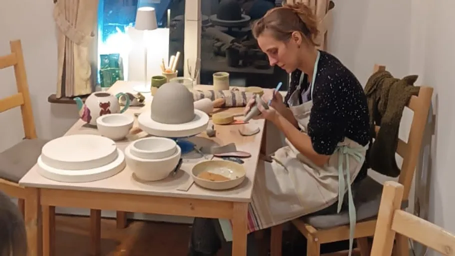 Potter working on ceramics at indoor table.