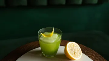 Green cocktail with lemon garnish on table.