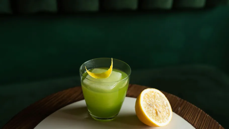 Green cocktail with lemon garnish on table.