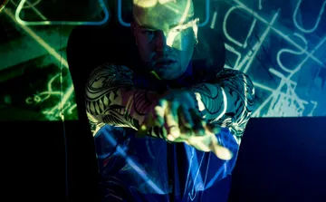 Man with tattoos in colorful light display.