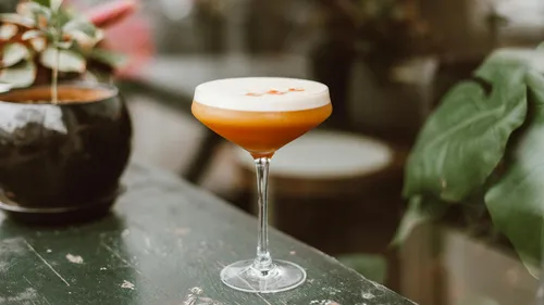 Glas mit Cocktail auf rustikalem Tisch draußen.