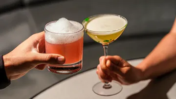 Two hands clinking colorful cocktails together.