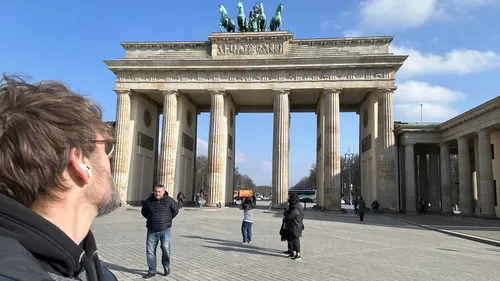 Man with earbuds looks at Brandenburg Gate.