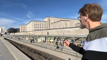 Mann zeigt auf historischen Ausstellungsbereich im Freien.