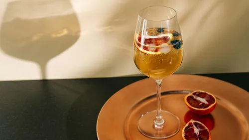 Weinglas mit Fruchtscheiben auf goldenem Tablett.