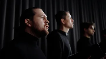 Men singing in a dark room, wearing black.