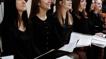 Group of women singing, holding music sheets.
