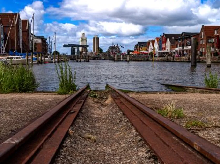 Rails end in water, surrounded by buildings and boats.