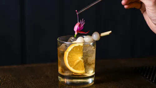 Cocktail with orange slice and flower garnish.
