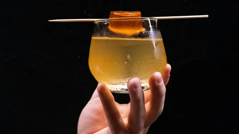 Hand holding cocktail with orange garnish.