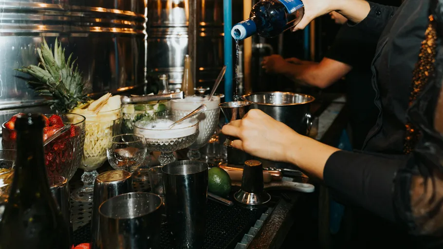 Person gießt Alkohol in Messbecher an Bar.