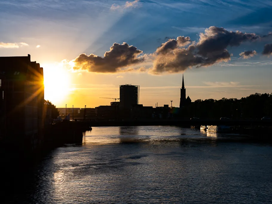 Sonnenuntergang über dem Fluss, umgeben von Stadtgebäuden.