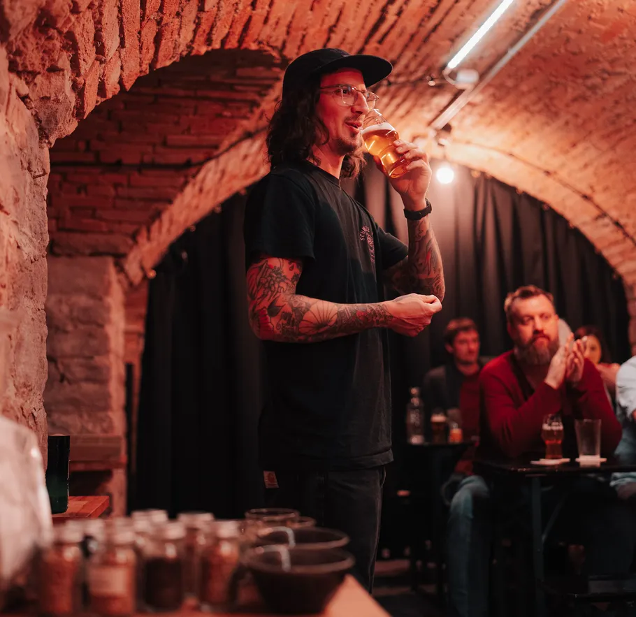 Man in a cellar drinking beer, audience watching.