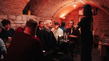 Personen sitzen und sprechen in einem schwach beleuchteten Backsteinraum.