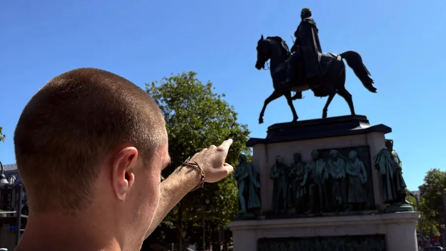 Person zeigt auf eine Reiterstatue im Freien.