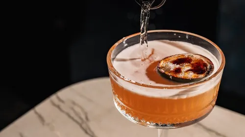 Cocktail being poured in a glass, marble table.