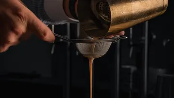 Bartender straining cocktail into glass using strainer.