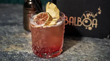 Cocktail with lime and pineapple garnish on table.
