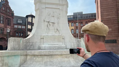 Mann fotografiert Denkmal mit Smartphone in Stadt.