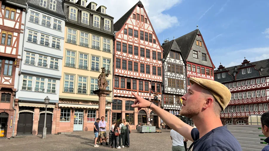 Mann zeigt auf historische Gebäude auf einem Platz.