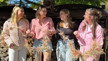 Vier Frauen lächeln, halten dekorative Kränze im Freien.